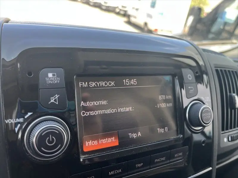 Gros plan sur l'écran multimédia noir du tableau de bord du Peugeot Boxer FGN blanc, affichant la radio FM Skyrock et l'autonomie.