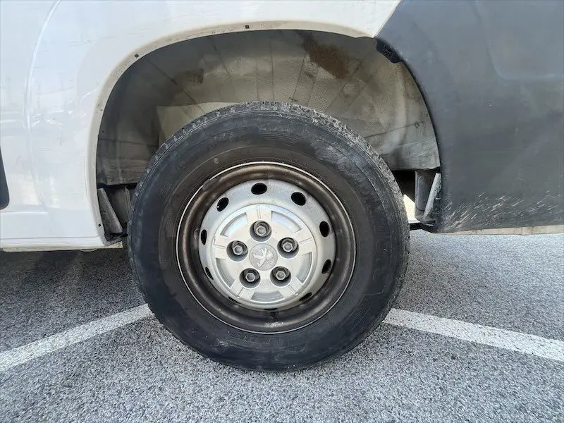 Gros plan sur la roue avant droite d'un Peugeot Boxer blanc de 2021, avec jante acier et logo Peugeot central.