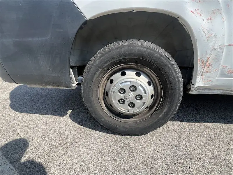 Gros plan sur la roue avant gauche du Peugeot Boxer blanc avec jante acier et traces d'usure sur la carrosserie.
