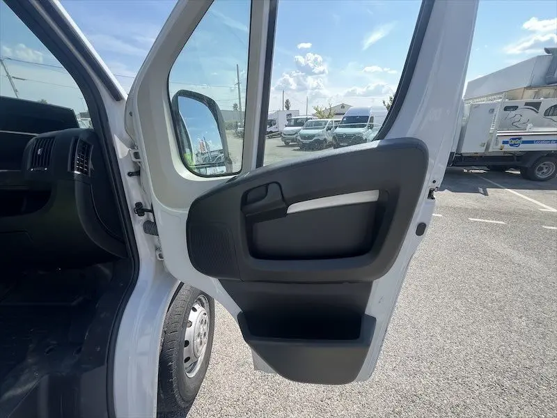 Vue intérieure de la porte avant gauche ouverte d’un Peugeot Boxer blanc, montrant la poignée et le panneau noir.