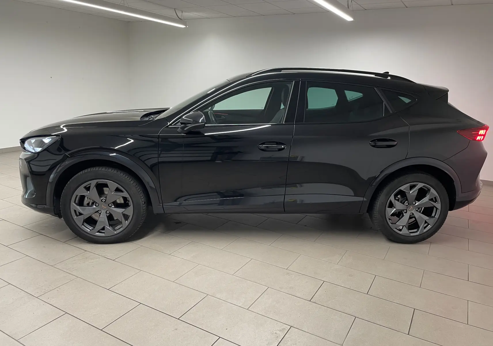 Vue de profil côté gauche du CUPRA Formentor 2.0 TDI 150 DSG7 en noir minuit avec feux arrière allumés dans un intérieur neutre.