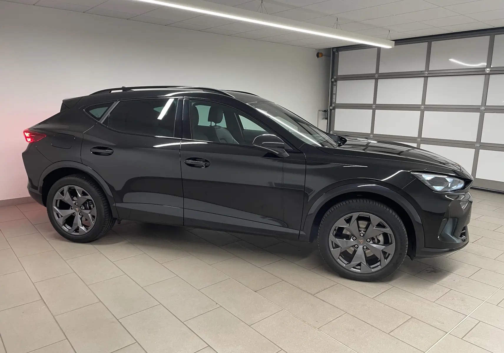 Vue de profil côté gauche d'un CUPRA Formentor 2025 noir minuit avec jantes foncées dans un garage intérieur.