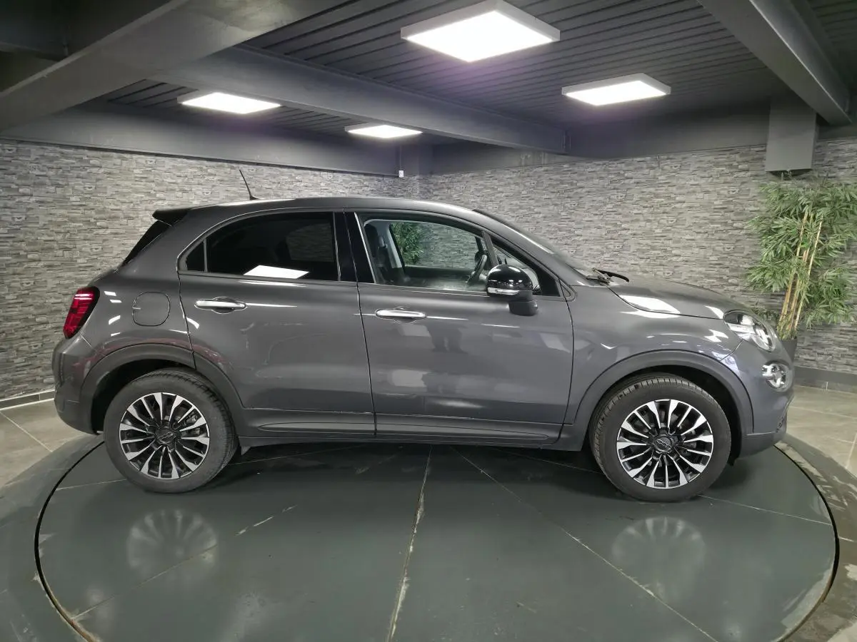 Profil droit d'un Fiat 500X gris avec jantes alliage 17'' et vitres surteintées en intérieur showroom.