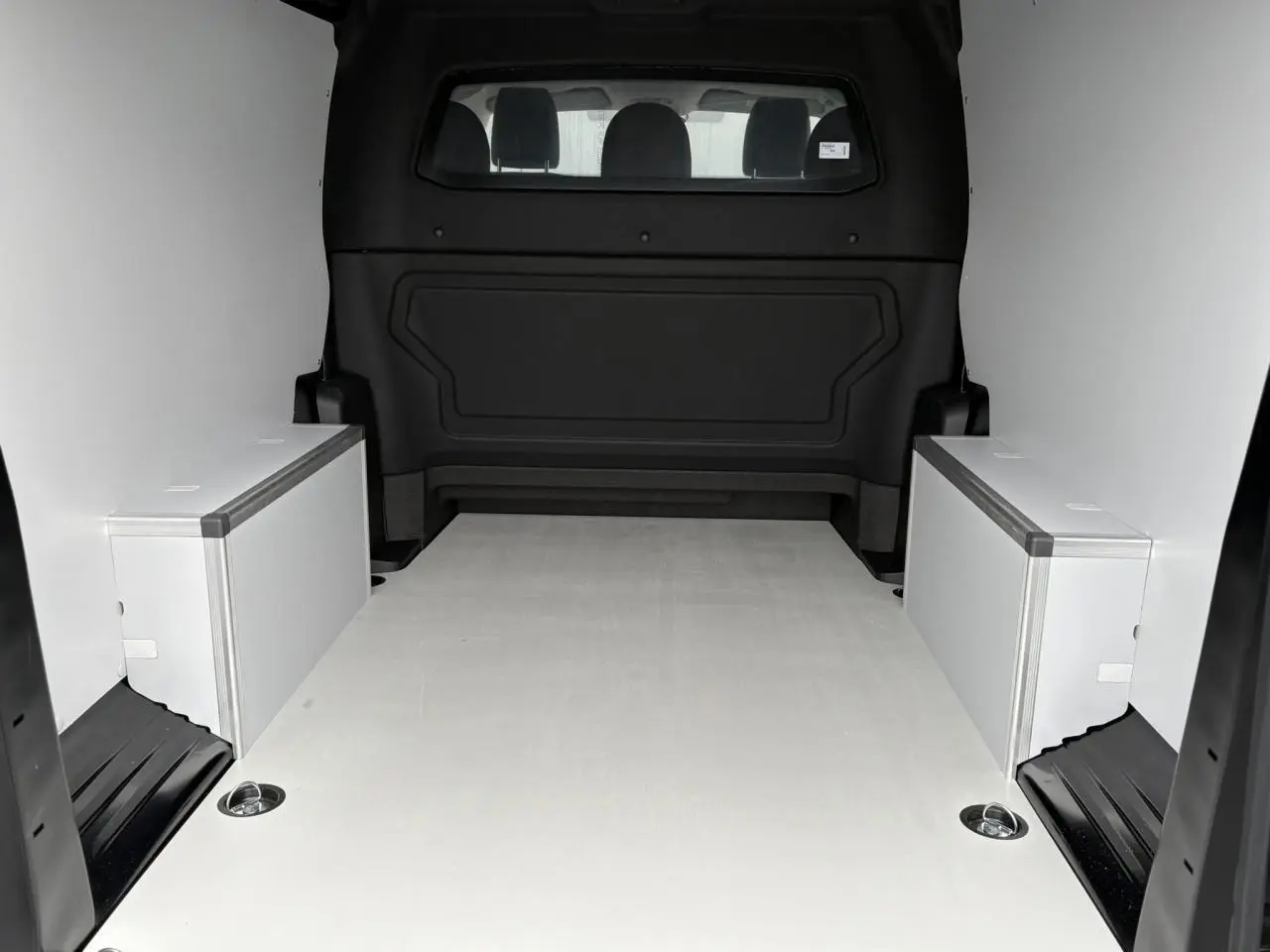 Vue intérieure arrière du Citroën Jumpy XL noir Perla montrant l’espace de chargement avec plancher bois et coffrages latéraux blancs.