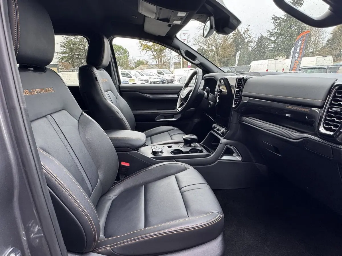 Vue intérieure côté conducteur du Ford Ranger Wildtrak 2025, sièges noirs avec surpiqûres orange et tableau de bord moderne.