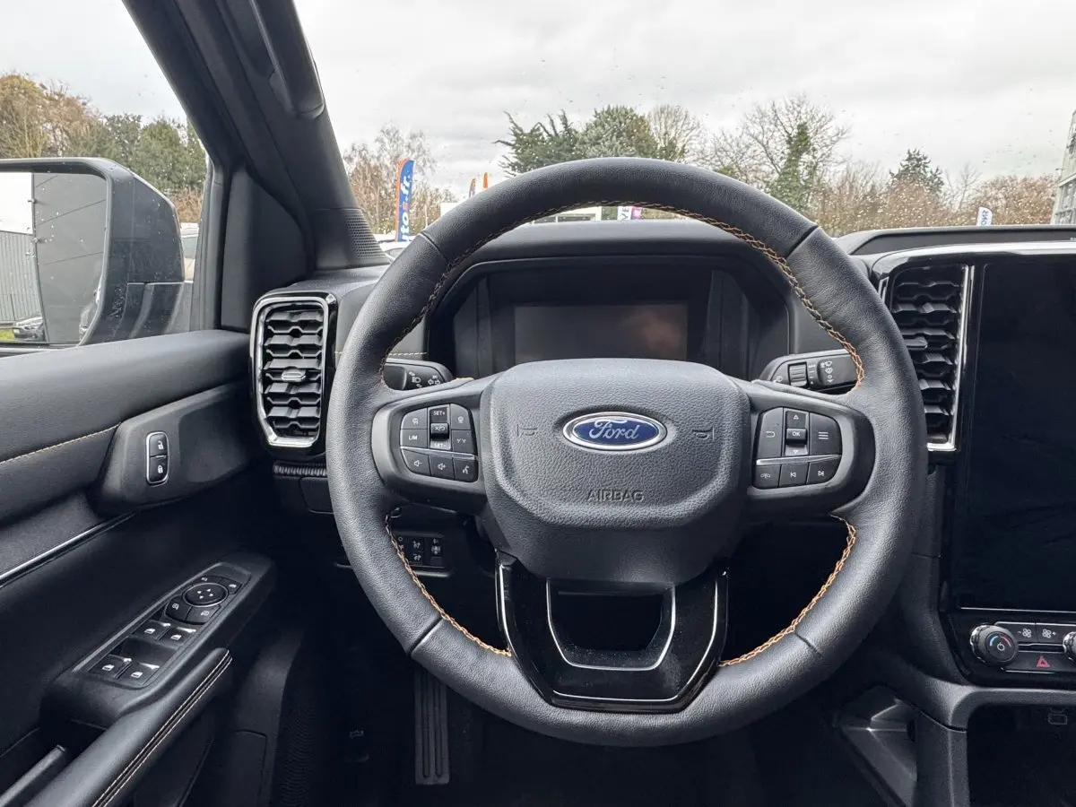 Vue intérieure centrée sur le volant cuir noir avec surpiqûres marron du Ford Ranger 2025, tableau de bord et écran tactile visibles.