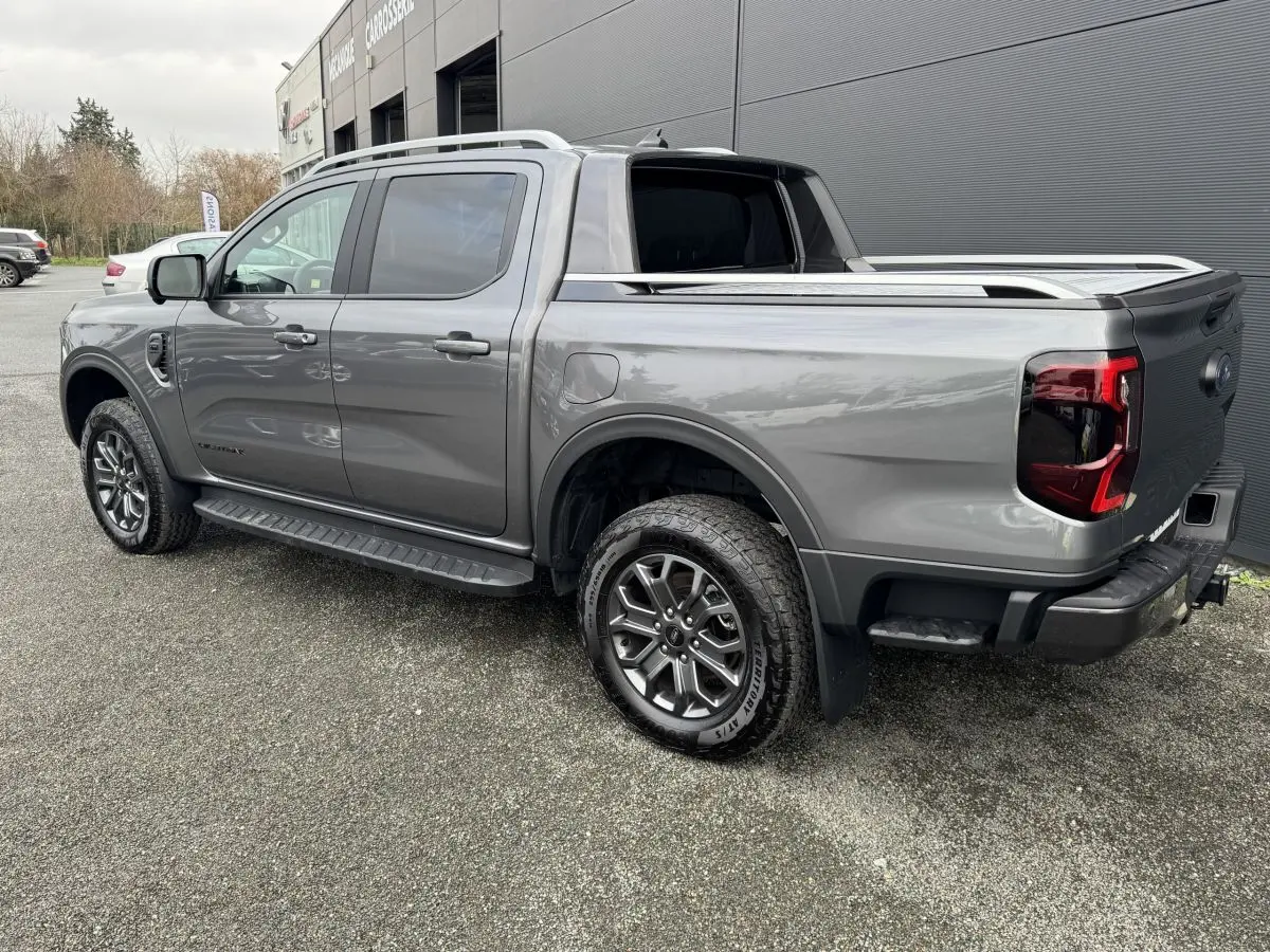 Vue 3/4 arrière droite d'un Ford Ranger gris métallisé avec benne, jantes alliage et marchepieds latéraux.