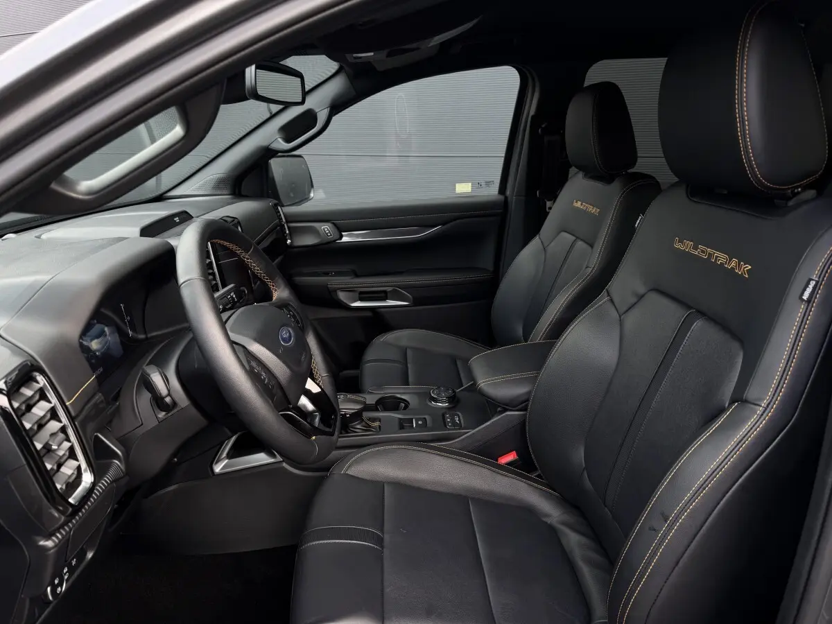 Vue intérieure côté conducteur du Ford Ranger Wildtrak 2025, sièges noirs avec surpiqûres orange et logo Wildtrak brodé.