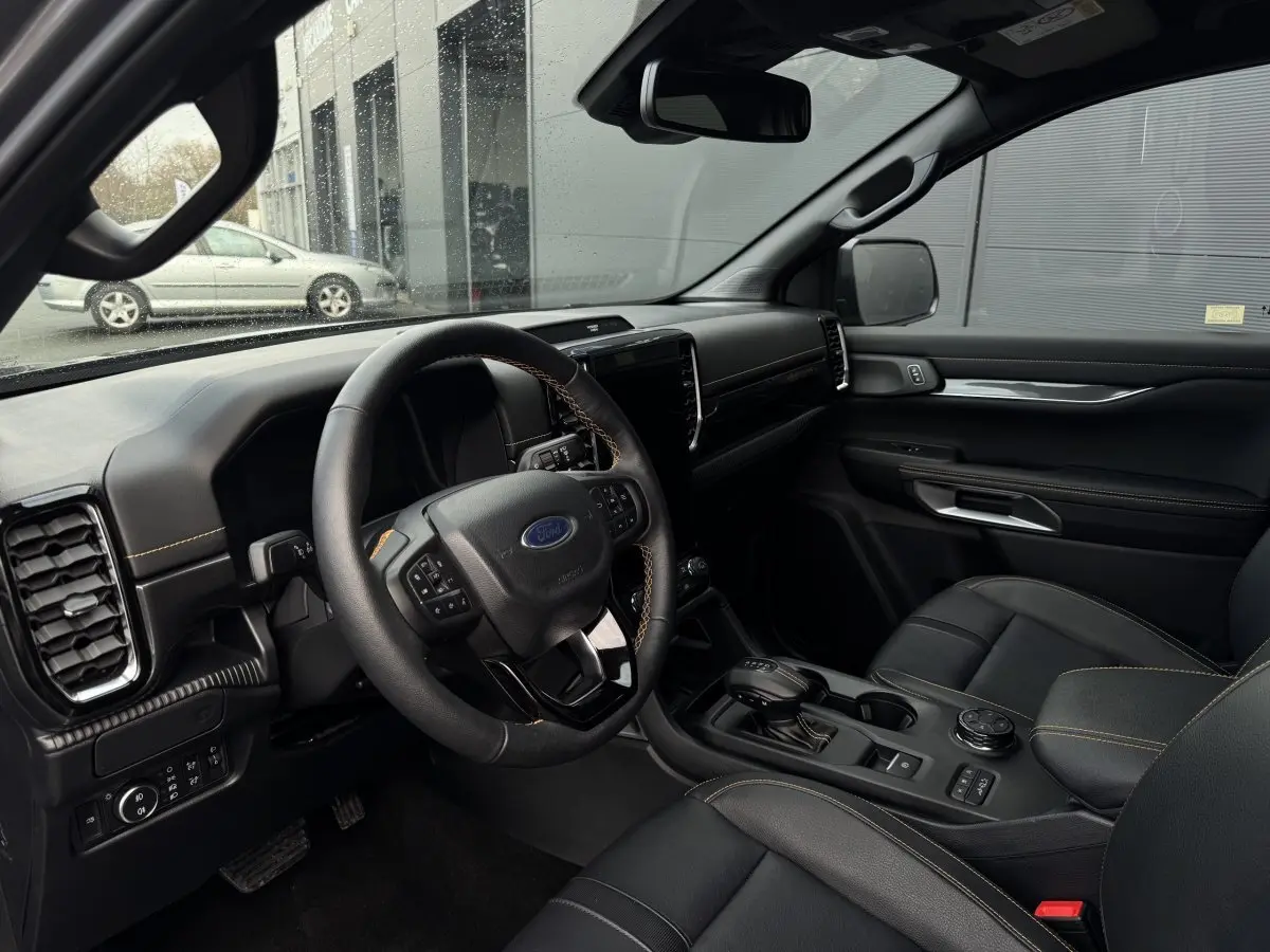 Vue intérieure côté conducteur du Ford Ranger 2025, tableau de bord noir avec coutures jaunes et écran tactile central.