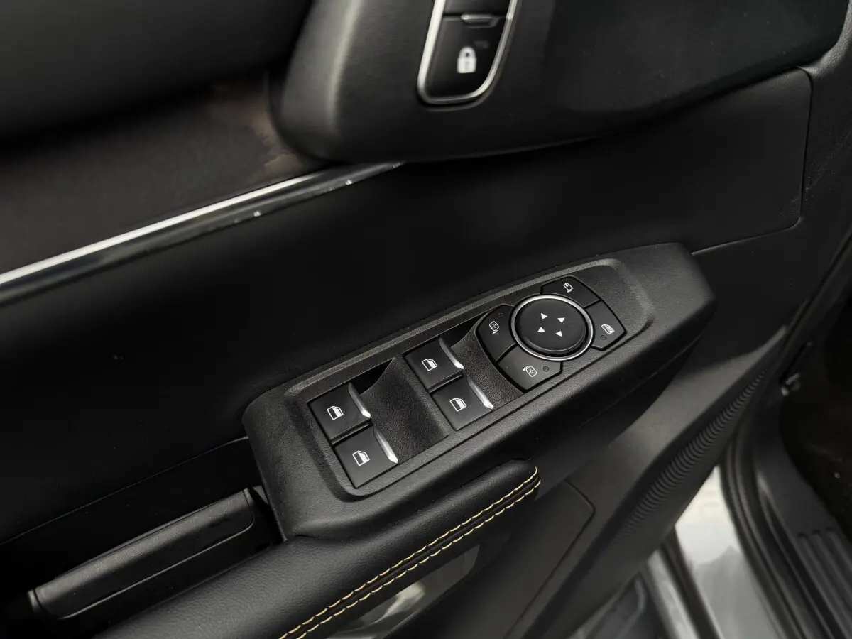 Gros plan sur la commande des vitres et rétroviseurs côté conducteur, garniture noire avec surpiqûres jaunes.