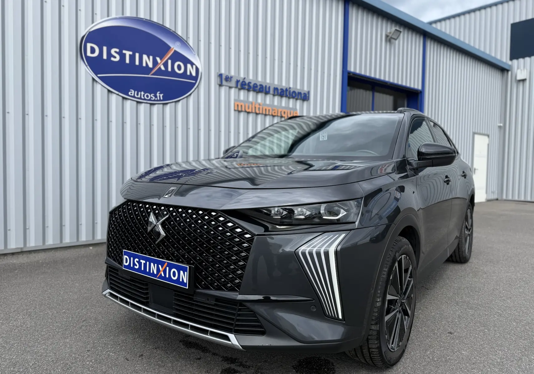 DS7 BlueHDi 130 Pallas gris titane en 3/4 avant droit, avec calandre distinctive et feux LED verticaux.