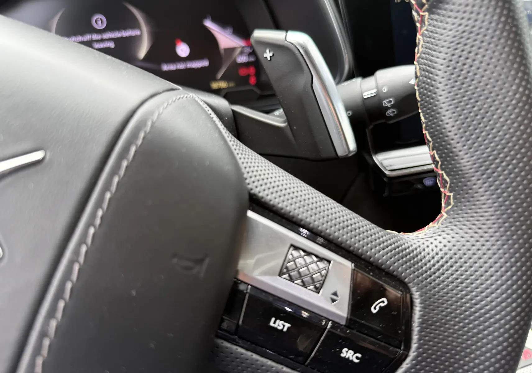 Gros plan sur le volant en cuir perforé avec surpiqûres rouges du DS7 2025, montrant les commandes intégrées.