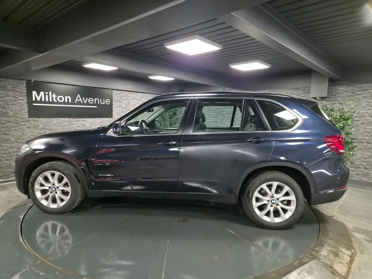 BMW X5 sDrive 25d bleu métallisé vue de profil côté gauche avec jantes alliage 19 pouces en intérieur showroom.