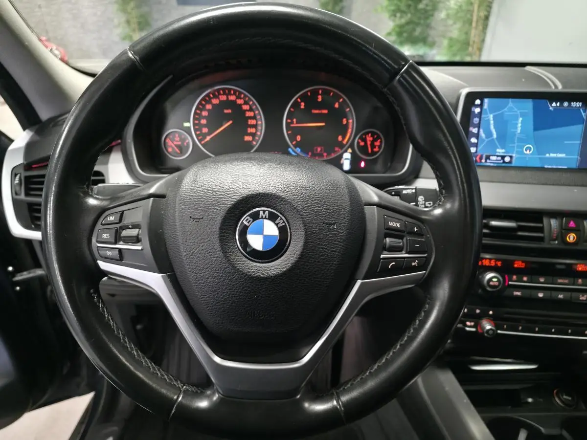Vue rapprochée du volant cuir noir BMW avec tableau de bord et écran de navigation dans un X5 sDrive 25d 2018.