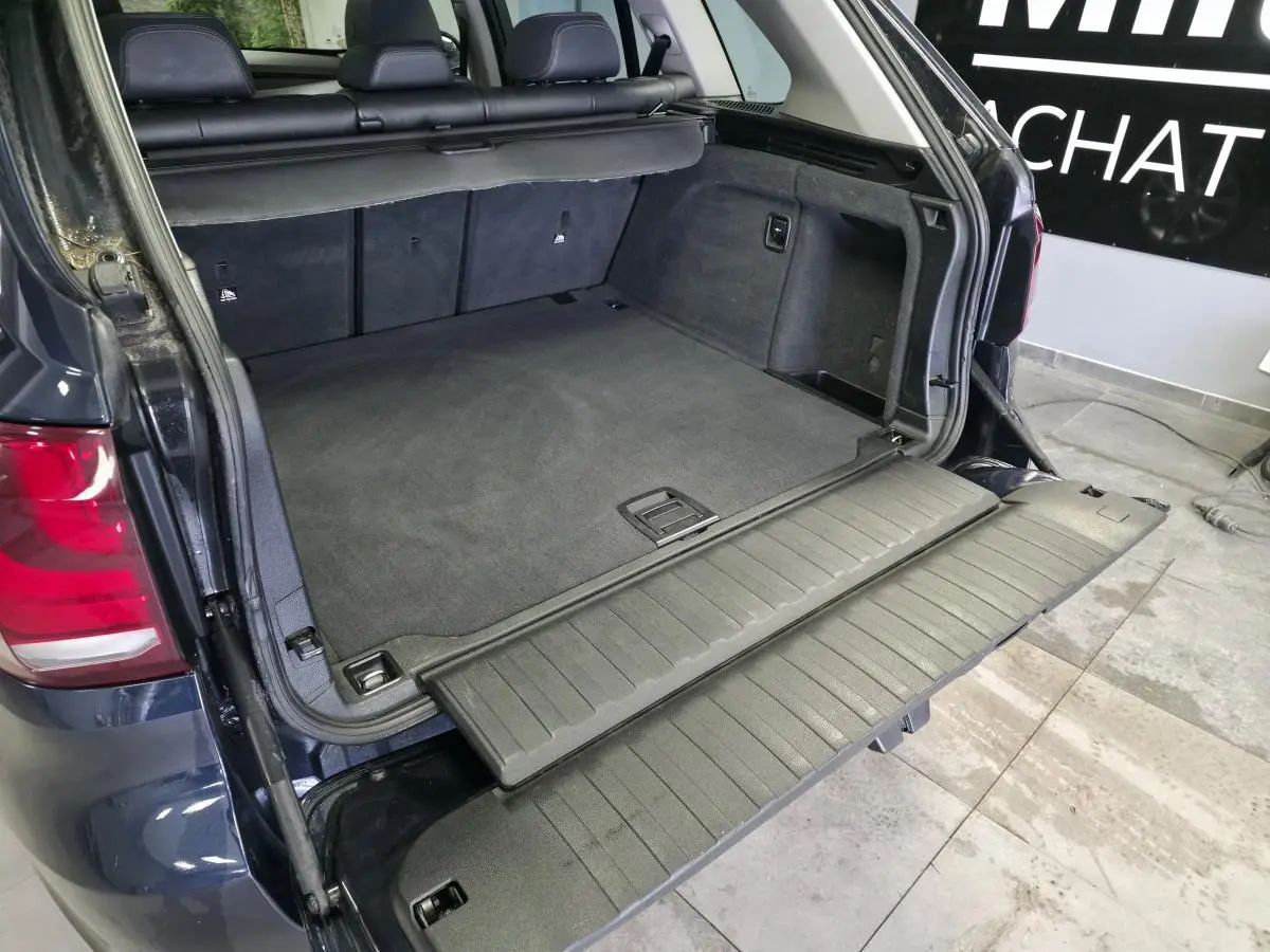 Coffre ouvert vu de l'arrière d'un BMW X5 sDrive 25d bleu avec plancher de chargement déplié et sellerie noire.