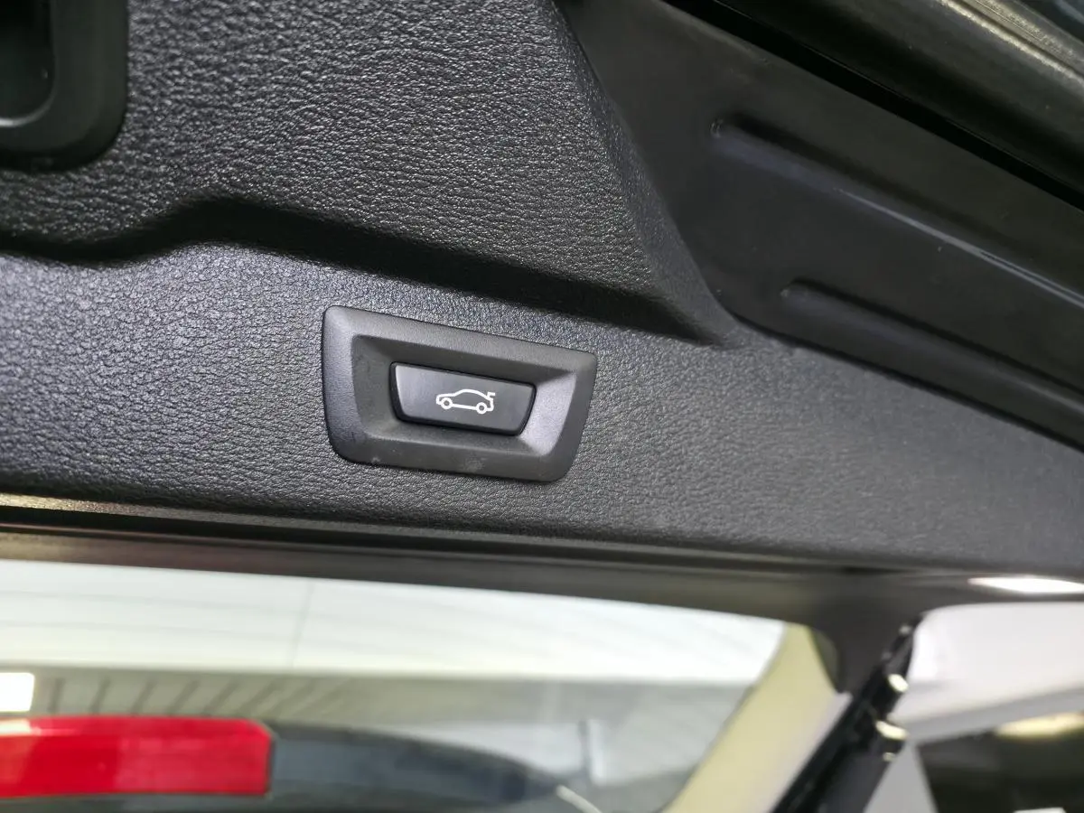 Bouton d'ouverture électrique du hayon vu en gros plan sur le bord intérieur du coffre d'un BMW X5 bleu 2018.