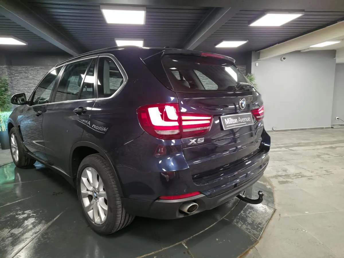 Vue 3/4 arrière droite d'un BMW X5 bleu métallisé avec crochet d'attelage et jantes alliage 19 pouces en showroom.