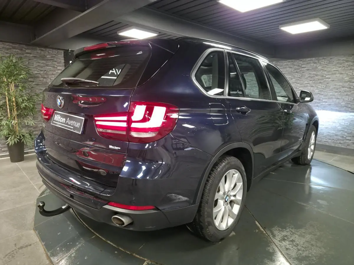 Vue 3/4 arrière droite d'un BMW X5 sDrive 25d bleu métallisé avec crochet d'attelage et jantes alliage 19 pouces.