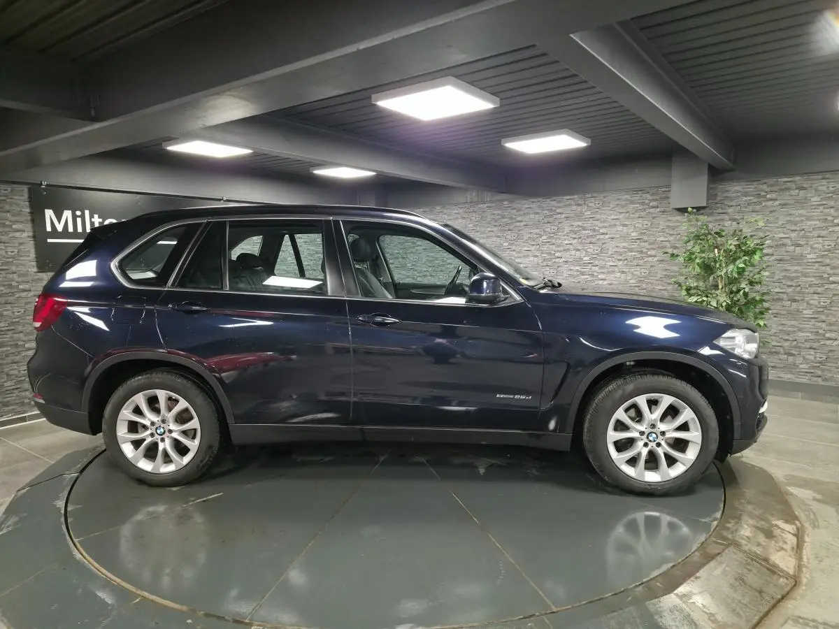 Profil droit d’un BMW X5 sDrive 25d bleu métallisé avec jantes alliage 19 pouces dans un showroom.