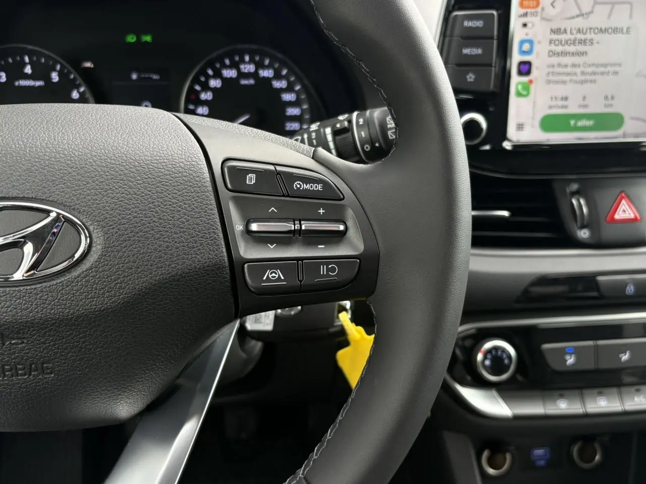 Gros plan sur le volant cuir noir de la Hyundai i30 SW T-GDI 120 Modern 2025, avec commandes intégrées et tableau de bord en arrière-plan.