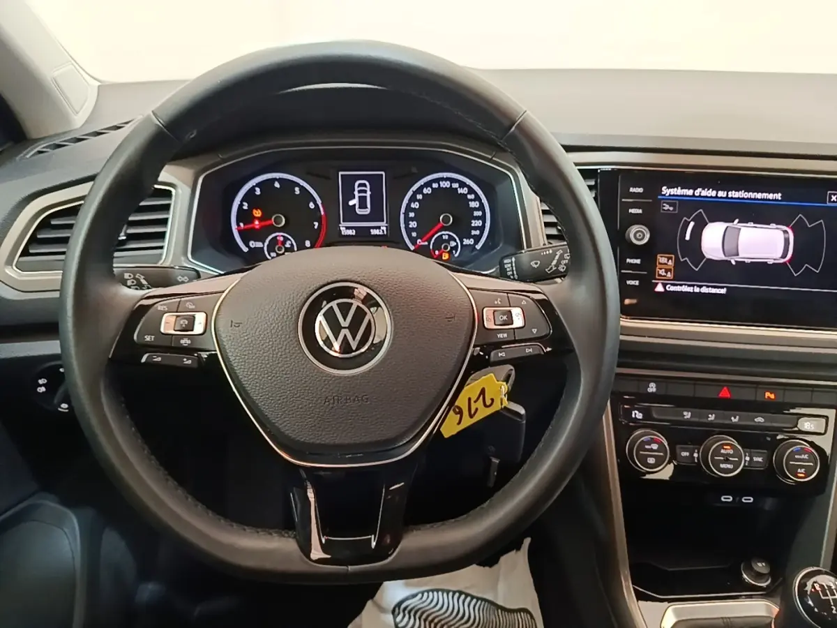 Vue intérieure centrée sur le volant cuir multifonctions d’un Volkswagen T-Roc 1.5 TSI avec tableau de bord digital et écran tactile.