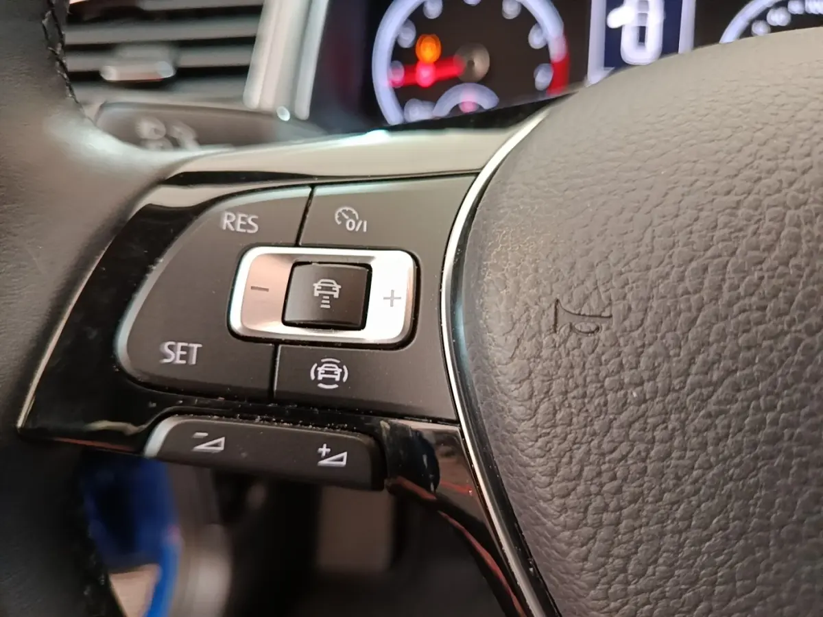 Gros plan sur les commandes du régulateur adaptatif au volant cuir noir du Volkswagen T-Roc bleu, tableau de bord en arrière-plan.