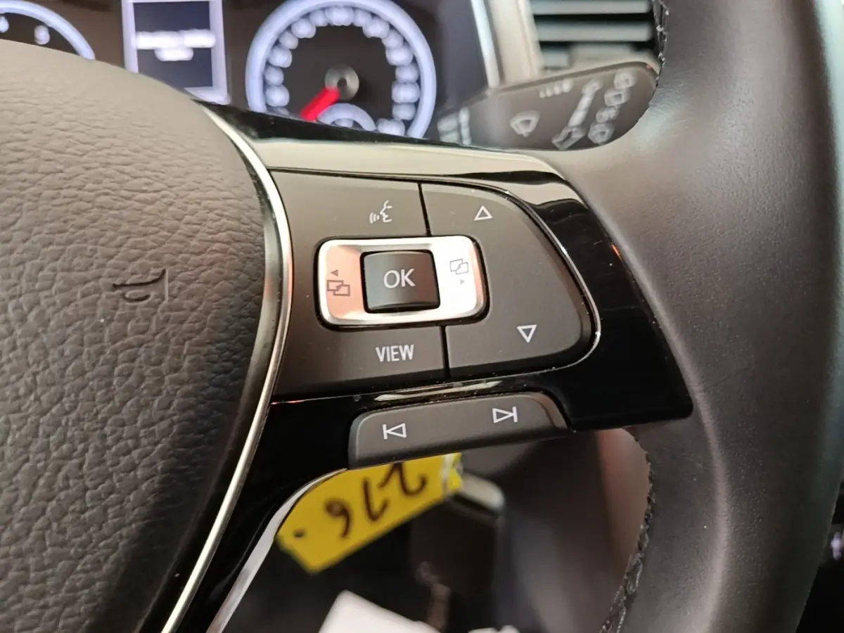 Gros plan sur les commandes multifonctions à droite du volant cuir noir du Volkswagen T-Roc 1.5 TSI bleu, tableau de bord en arrière-plan.