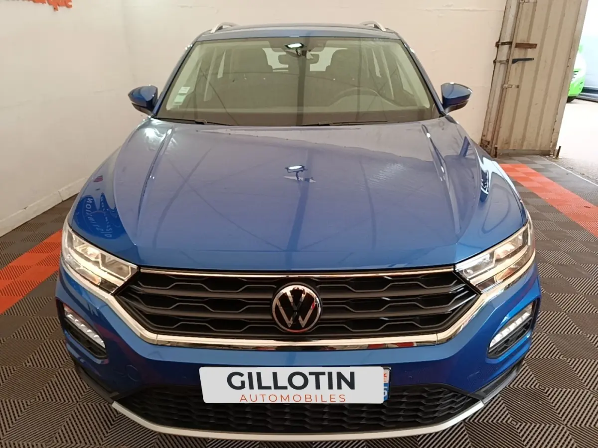 Vue avant d’un Volkswagen T-Roc bleu 2020 avec calandre noire et phares LED allumés dans un garage.