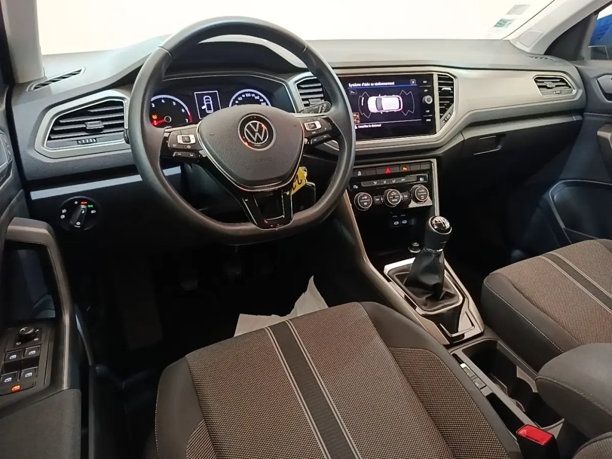 Vue intérieure avant du Volkswagen T-Roc 1.5 TSI bleu, volant cuir multifonctions et boîte manuelle visible.