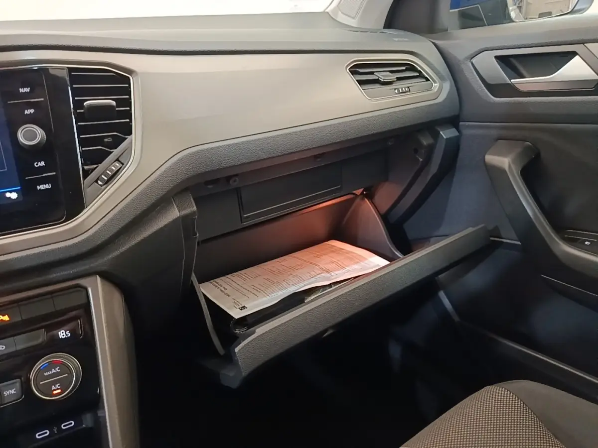 Vue intérieure côté passager du tableau de bord noir du Volkswagen T-Roc avec boîte à gants ouverte et documents visibles.