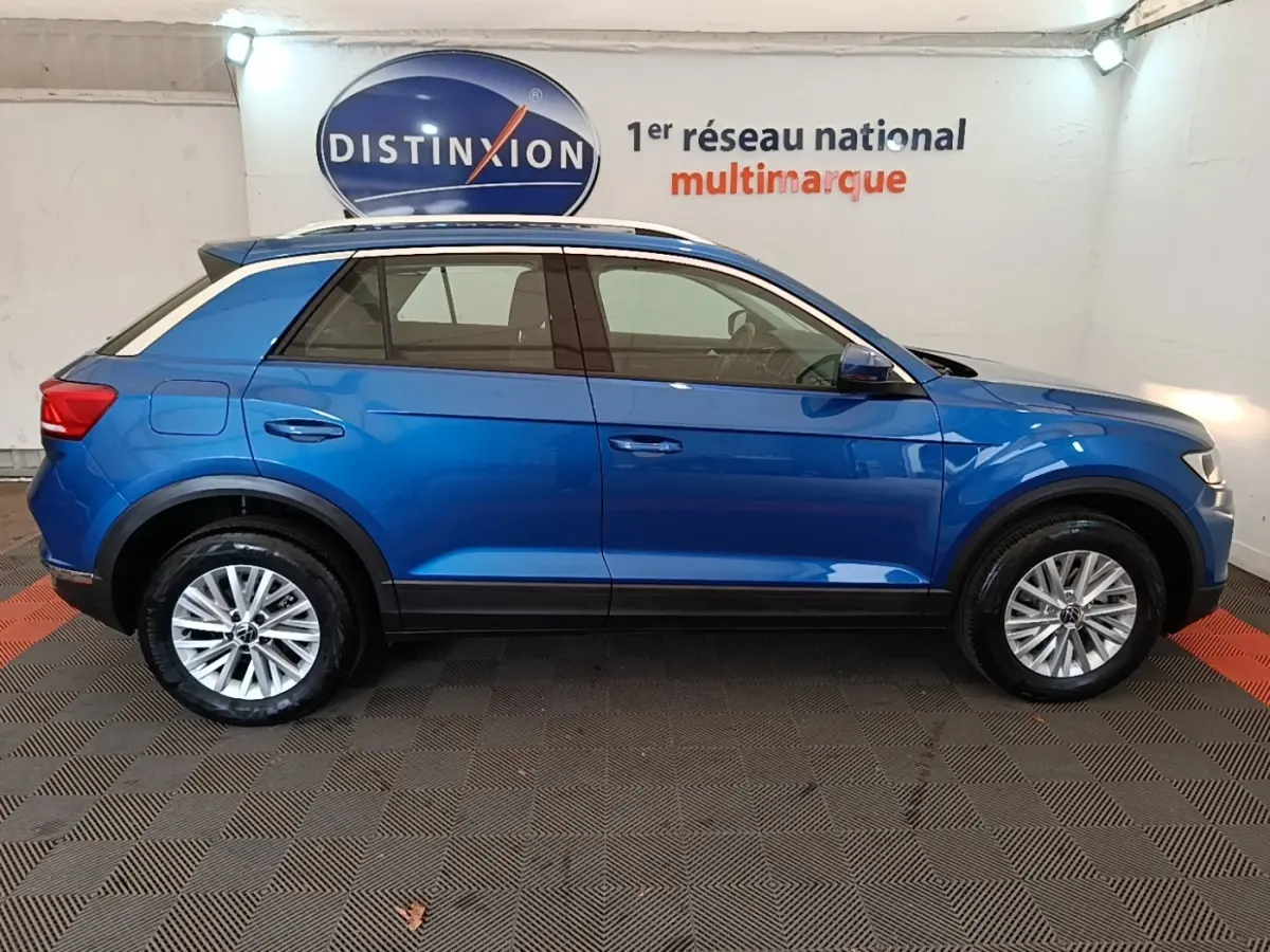 Profil droit d’un Volkswagen T-Roc bleu 2020 avec toit blanc et jantes alliage, en intérieur showroom.
