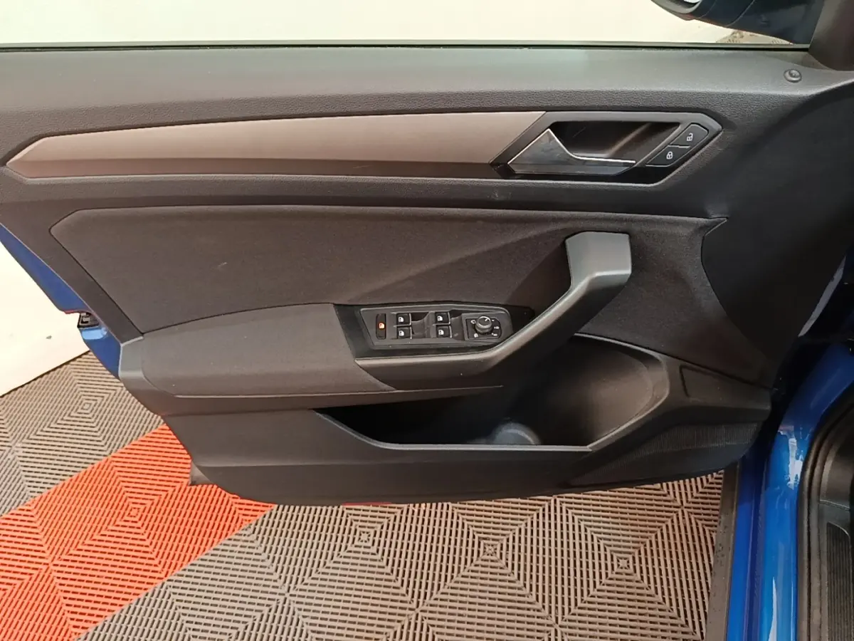 Vue latérale intérieure de la porte avant gauche du Volkswagen T-Roc bleu, avec commandes électriques des vitres et verrouillage.