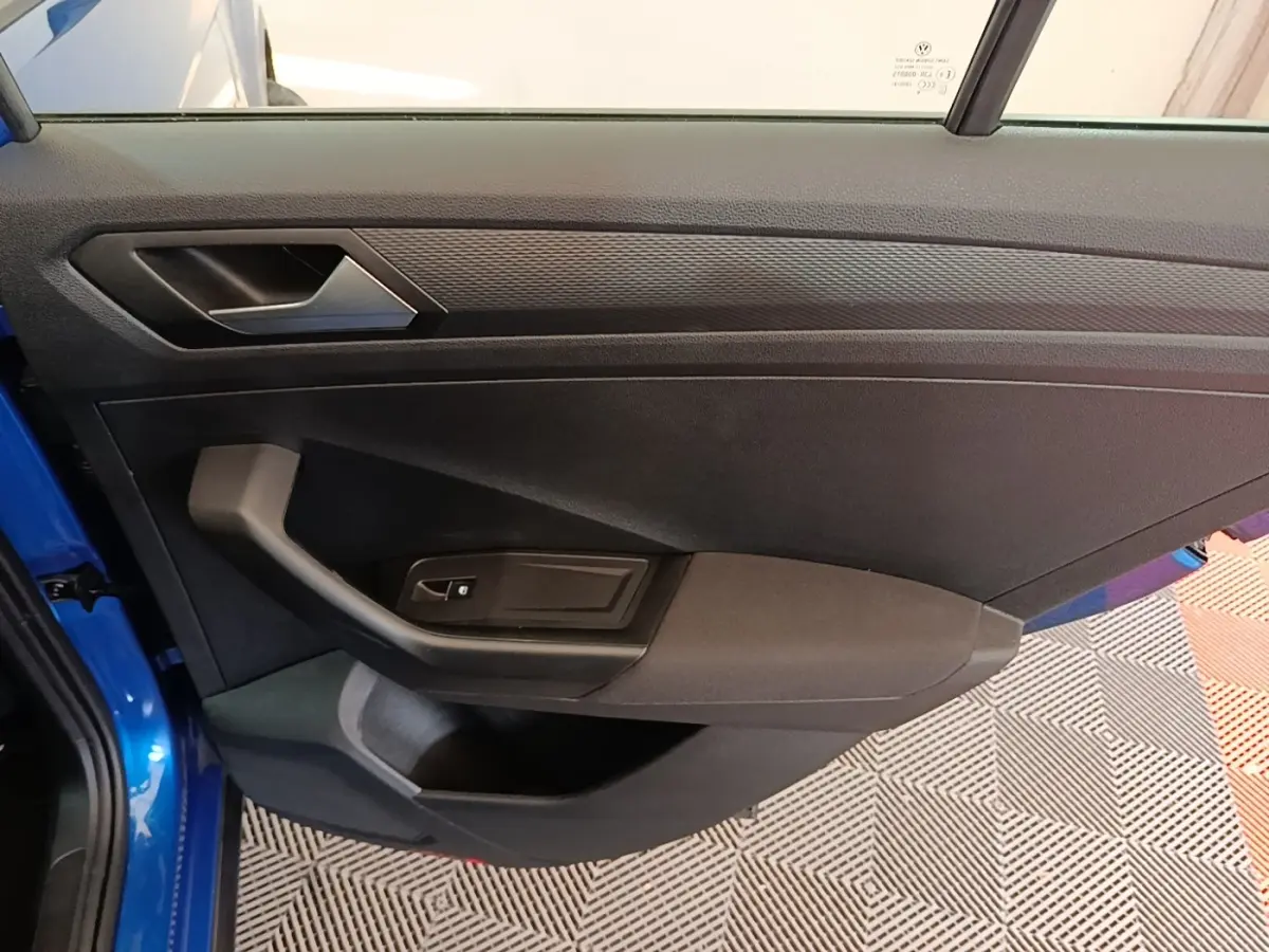 Vue rapprochée de la porte avant gauche bleu vif du Volkswagen T-Roc 1.5 TSI avec poignée et commande de vitre noire.