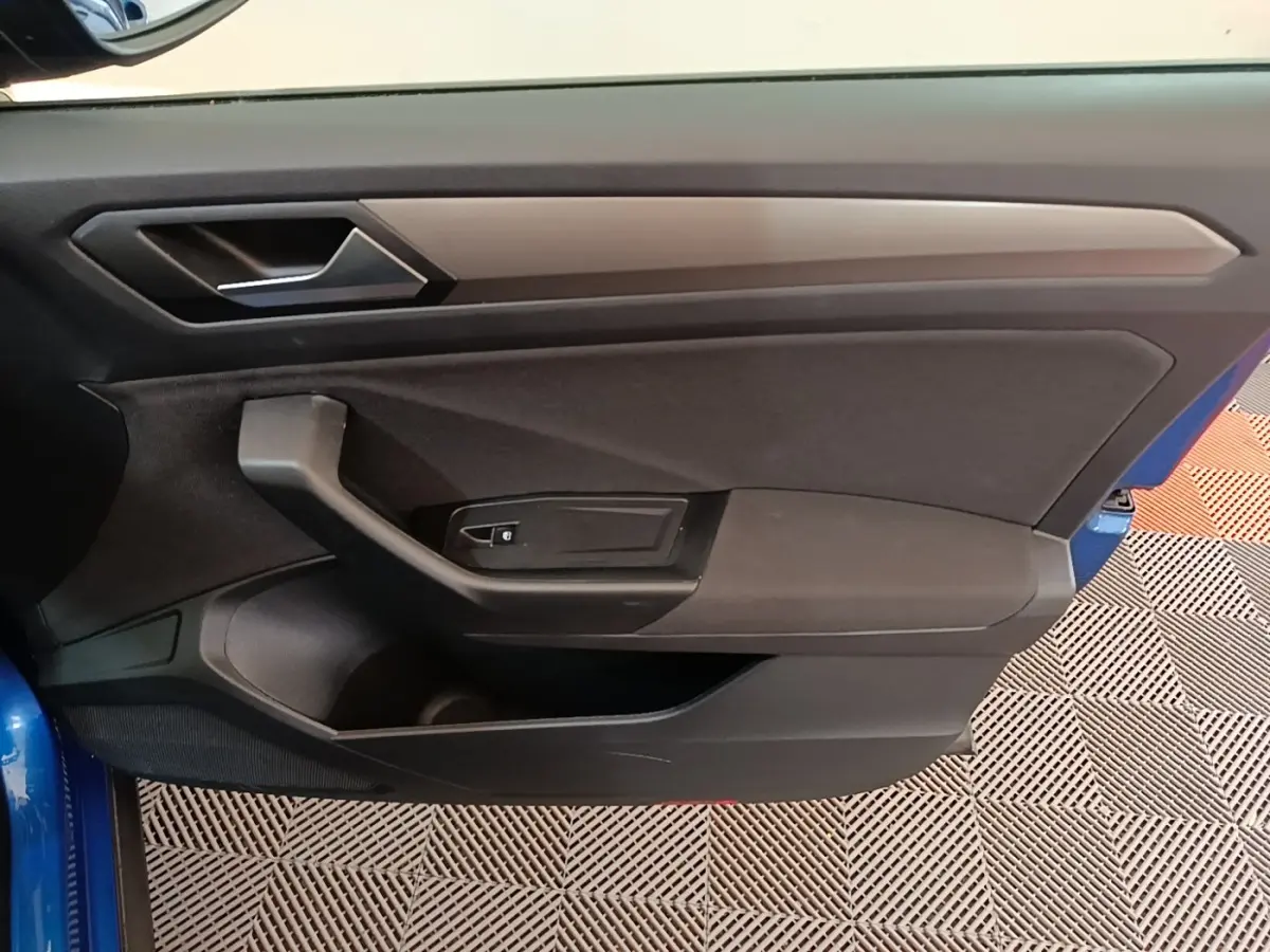 Vue intérieure de la porte avant gauche d’un Volkswagen T-Roc bleu, avec poignée et commande de vitre noire.