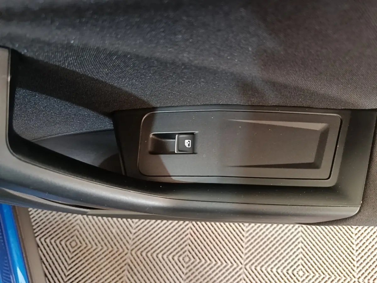 Détail de la commande d’ouverture de coffre sur la porte intérieure d’un Volkswagen T-Roc bleu.