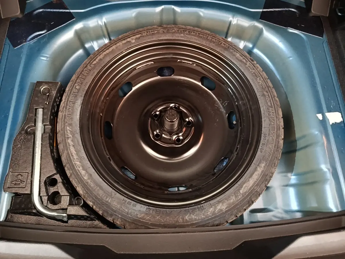 Roue de secours noire dans le coffre bleu d’un Volkswagen T-Roc 1.5 TSI 150 EVO UNITED, vue de dessus.