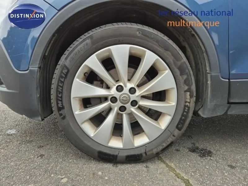 Gros plan sur la roue avant gauche avec jante alu d’un Opel Mokka bleu outremer visible partiellement.