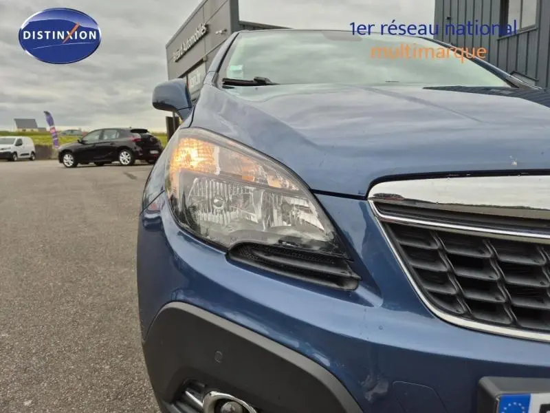 Gros plan sur l'avant gauche de l'Opel Mokka bleu outremer avec phare allumé et calandre chromée visible.