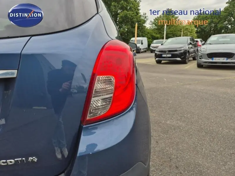 Gros plan sur le feu arrière droit d’un Opel Mokka bleu outremer, avec logo CDTI et reflet de l’environnement urbain.