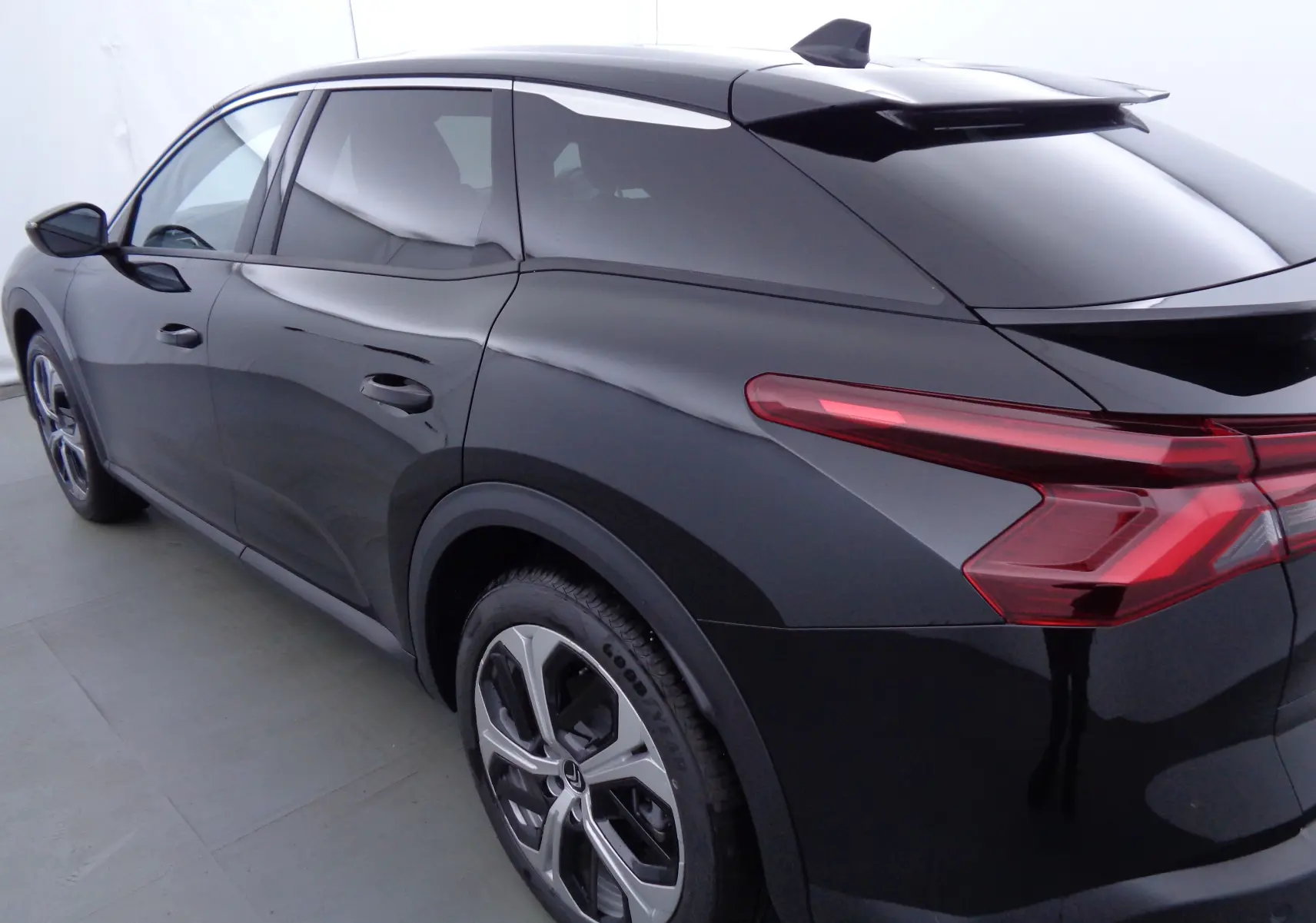 Vue 3/4 arrière côté gauche d'une Citroën C5 X noire métal avec feux arrière LED et jantes alliage bicolores.