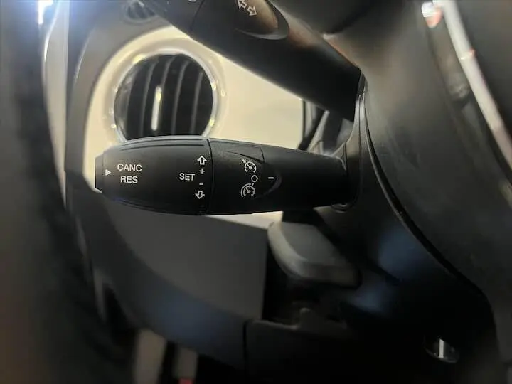 Gros plan sur la commande de régulateur de vitesse côté gauche du volant d'une Fiat 500 blanche 2023.