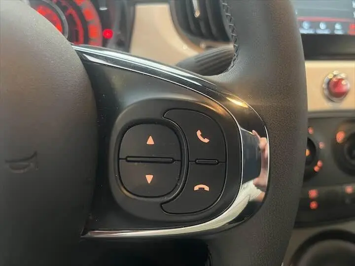 Gros plan sur les commandes de téléphone et volume au volant d'une Fiat 500 blanche, intérieur clair et moderne.