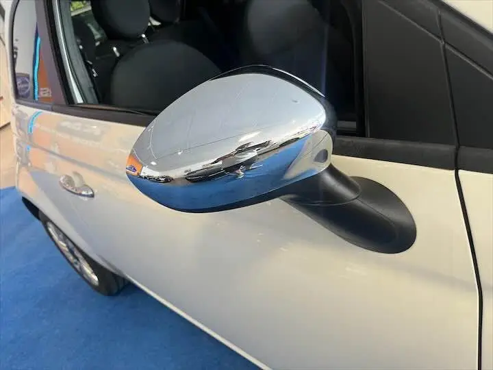 Rétroviseur chromé côté gauche d'une Fiat 500 blanche vue en gros plan sur fond bleu.