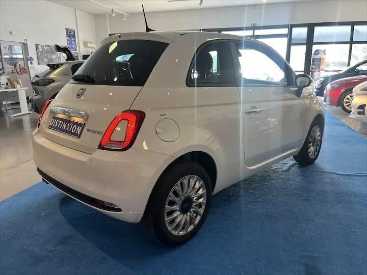 Vue 3/4 arrière droite d'une FIAT 500 blanche 2023 dans un showroom, avec jantes multi-branches et toit noir.
