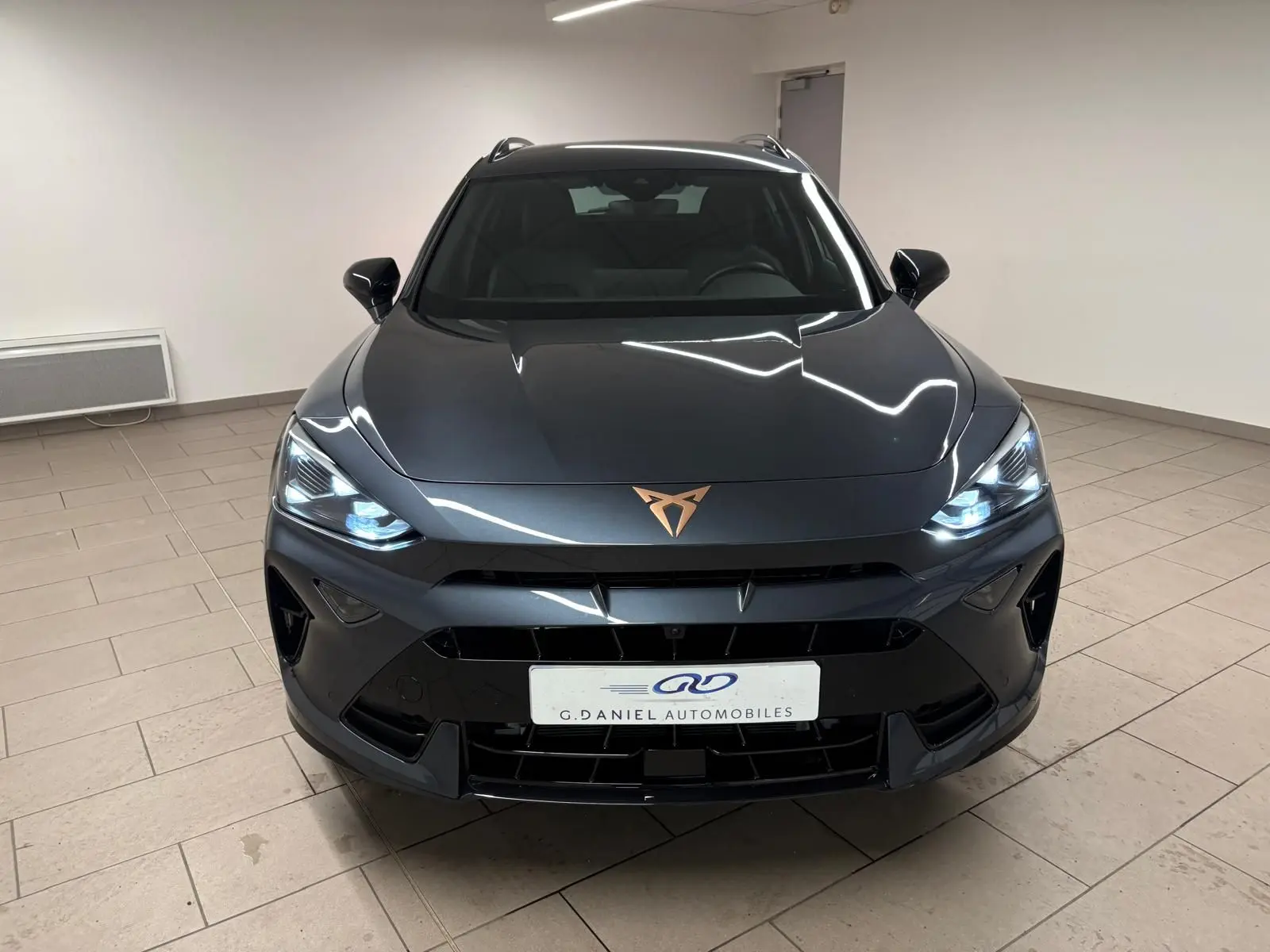 Vue frontale d'un CUPRA Formentor gris magnétique avec phares allumés et logo cuivré sur le capot.