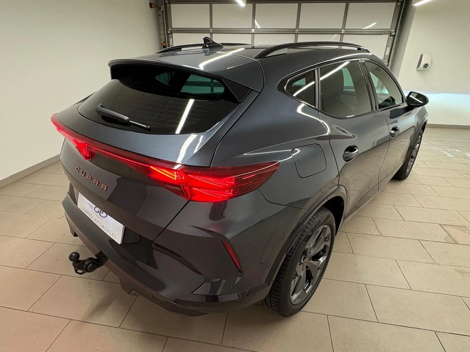 Vue 3/4 arrière droite d'un CUPRA Formentor gris magnétique avec attelage escamotable et feux arrière allumés.