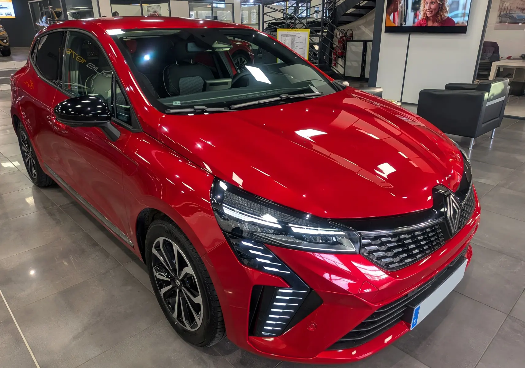 Renault Clio V ECO-100 CH TECHNO rouge flamme vue 3/4 avant droit en showroom avec détails LED avant.