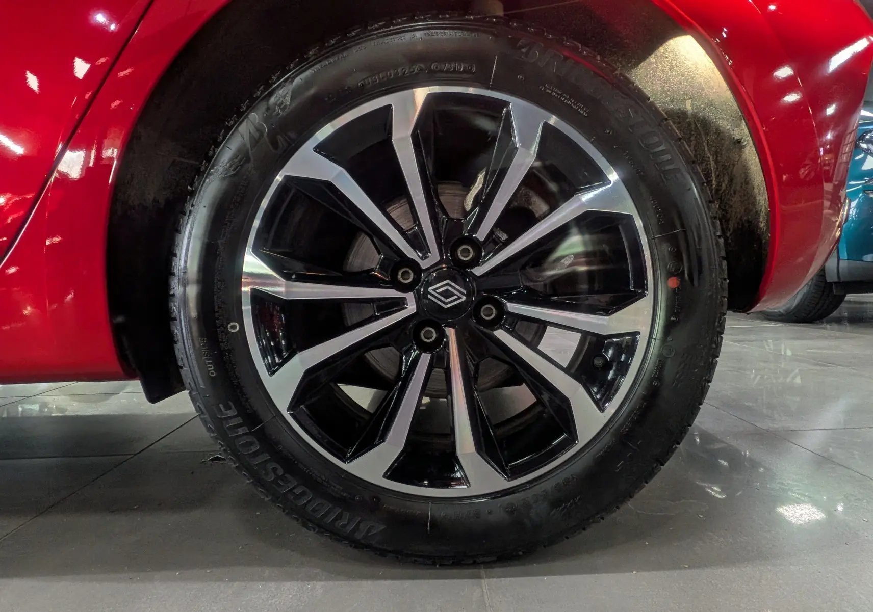 Gros plan sur la roue avant gauche de la Renault Clio V Rouge Flamme, mettant en valeur la jante noire et argentée au design moderne.