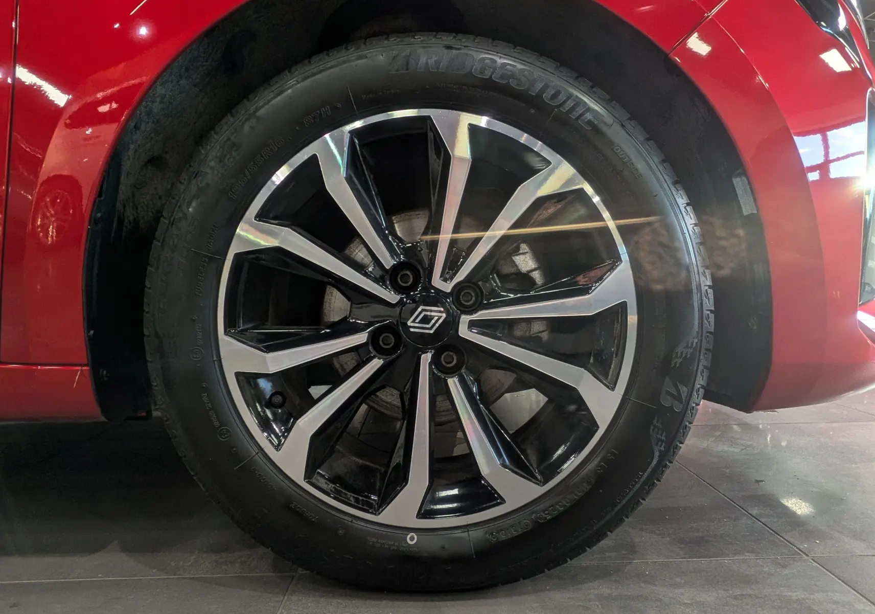 Gros plan sur la roue avant gauche de la Renault Clio V Rouge Flamme, jante alliage bicolore au design moderne.