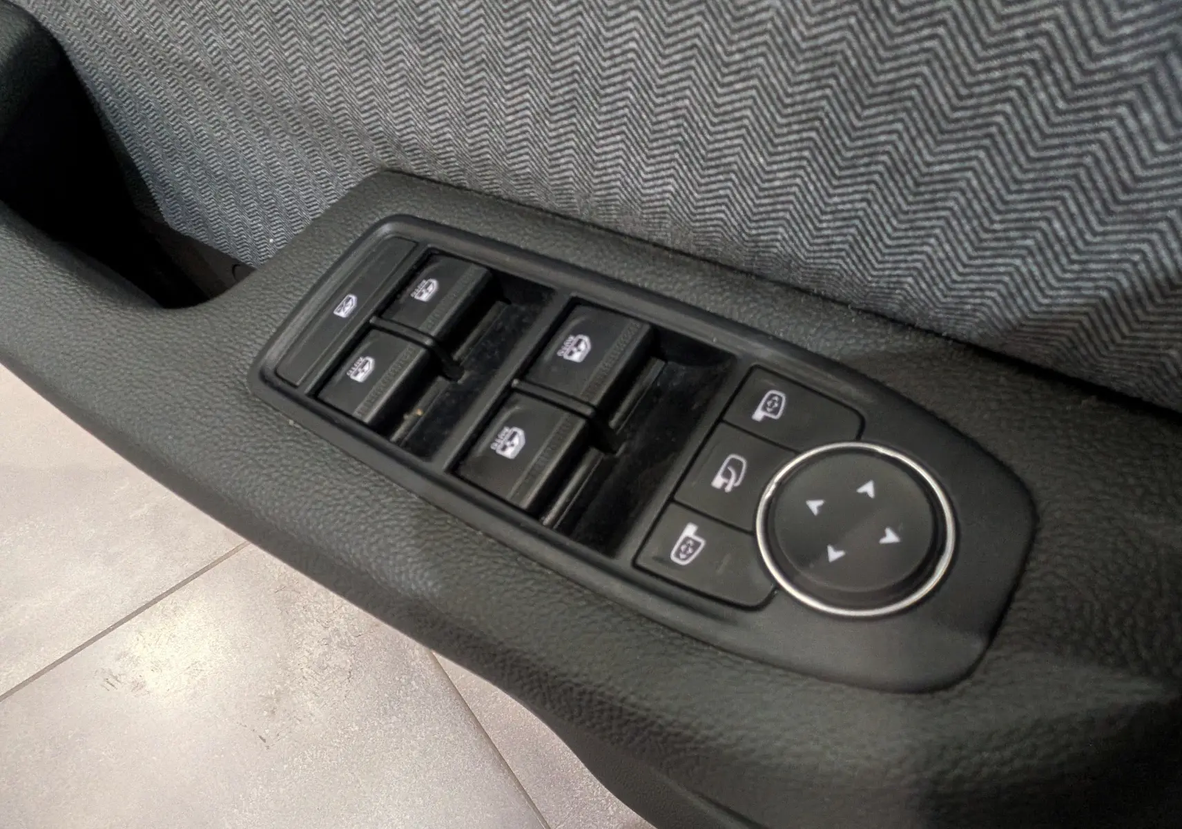 Gros plan sur les commandes des vitres et rétroviseurs côté gauche intérieur de la Renault Clio V rouge Flamme 2025.